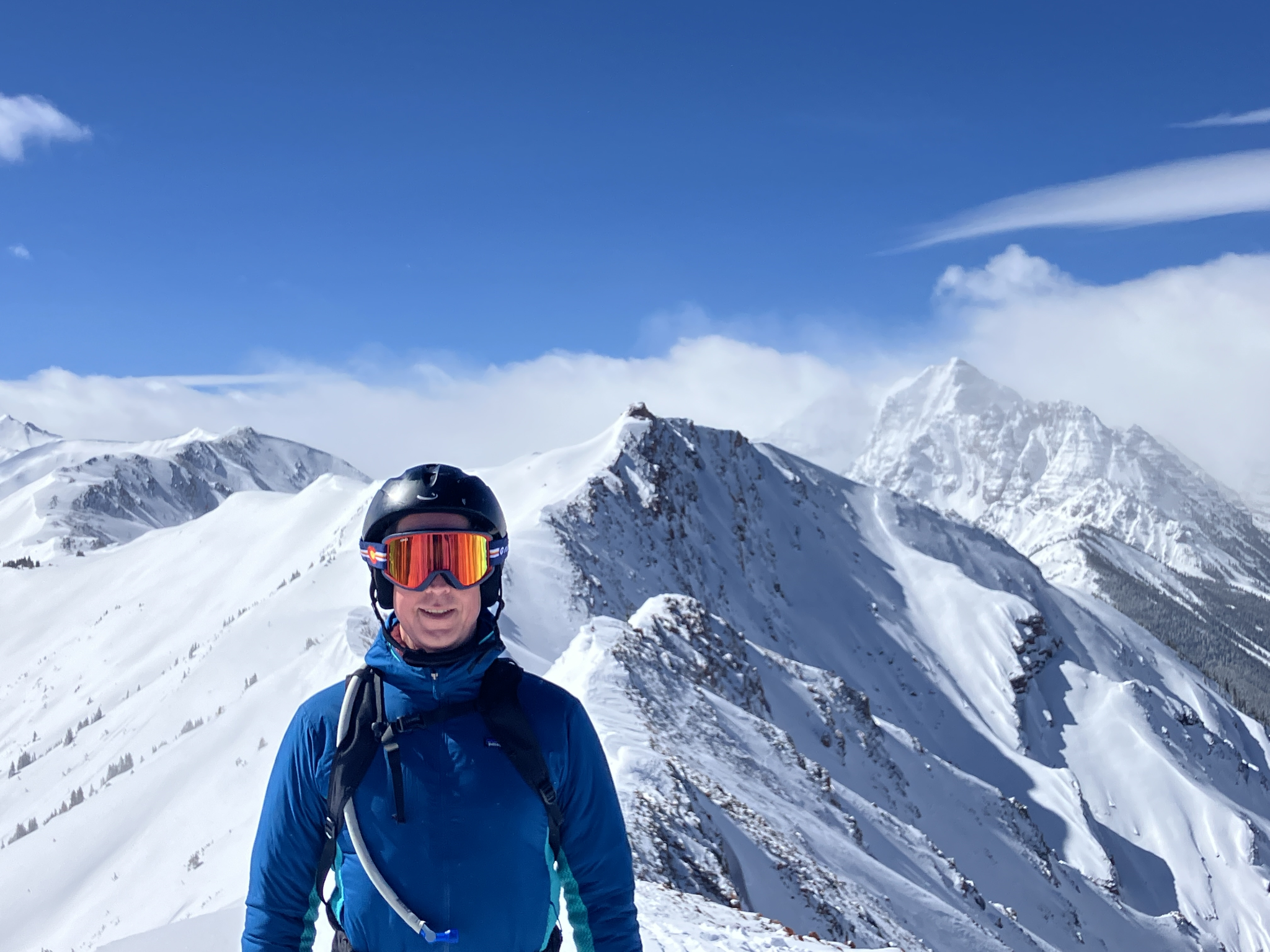 A skier on a snowy mountain ridge beneath a blue sky.